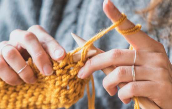 A close up view of someone knitting using a mustard coloured wool.