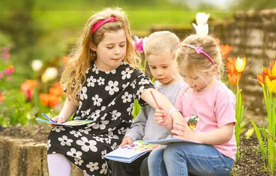 Three children sit on a wall looking at quest leaflet