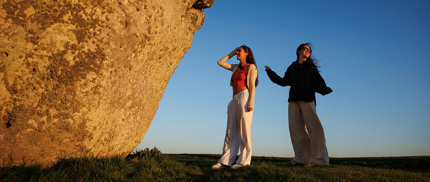Two people standing next to the Heel stone at Stonehenge