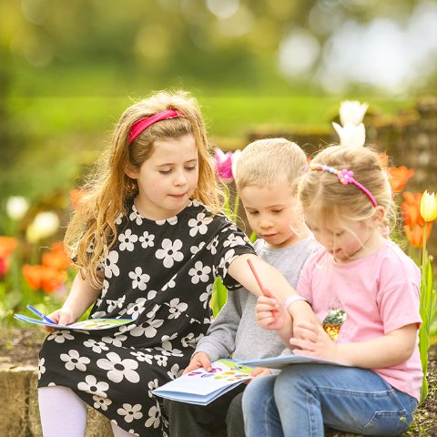 Three children sit on a wall looking at quest leaflet
